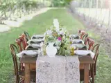 a vintage rustic wedding reception in a vineyard, with a lace table runner, bright blooms and greenery is a very welcoming idea