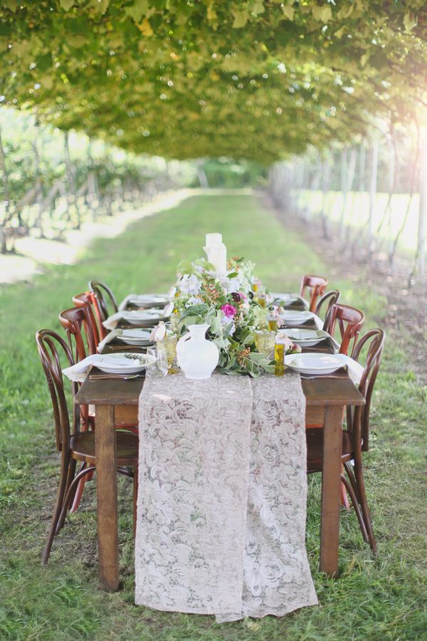 A vintage rustic wedding reception in a vineyard, with a lace table runner, bright blooms and greenery is a very welcoming idea