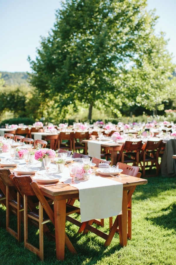 A vineyard wedding reception with greenery, neutral linens and pink blooms is a very cool and chic space with much natural light