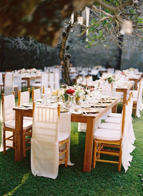 a bold vineyard wedding reception with stained furniture, bright and white blooms and greenery, white chair covers