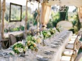 an exquisite neutral wedding reception with a tent, a beautiful tablescape with greenery and neutral blooms and vintage chandeliers over the table
