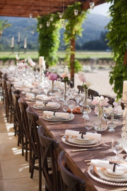 a chic vineyard wedding reception surrounded with greenery, with stained tables, white and pink blooms and pillar candles is a beautiful vintage-inspired space