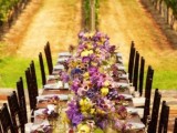 a bright vineyard wedding reception space with bold yellow and purple blooms and greenery, an uncovered table and gorgeous views of the vines