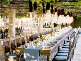 a chic vintage vineyard reception space with a dusty blue table runner and matching cushions on the chairs, bright blooms and greenery and crystal chandeliers