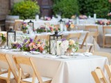a vineyard wedding reception with neutral tablecloths, bright blooms and greenery and candle lanterns and greenery around the space