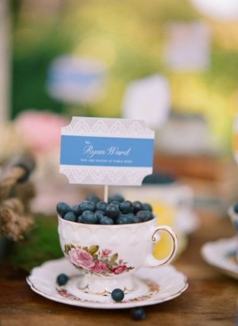 a vintage teacup filled with blueberries and with escort cards is a great wedding favor idea and escort card holder