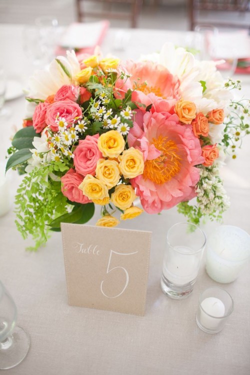 a bright summer wedding centerpiece of coral pink, orange, yellow and white blooms and greenery is a vivacious summer decoration