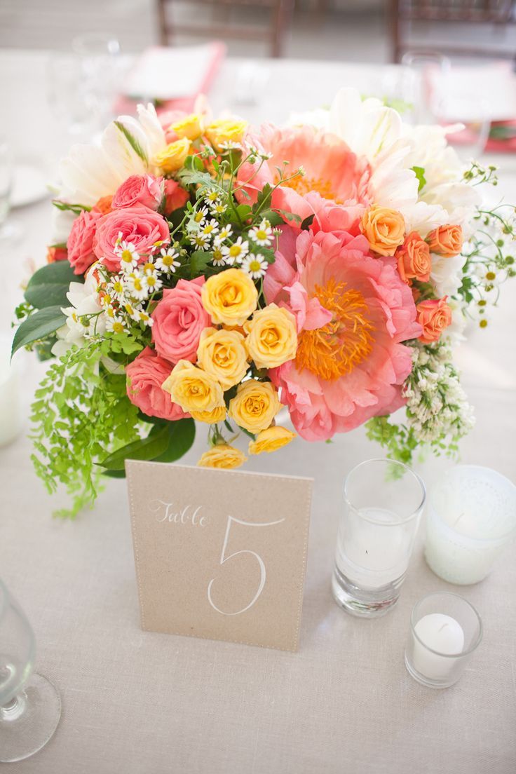 a bright summer wedding centerpiece of coral pink, orange, yellow and white blooms and greenery is a vivacious summer decoration