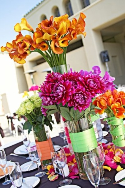 super bold summer wedding centerpieces of vases wrapped with ribbon and with fuchsia, orange, green blooms of various kinds