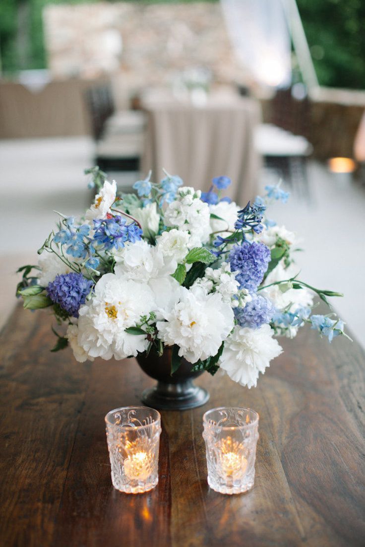 a beautiful wedding centerpiece of a black urn, white and blue blooms and some candles is a lovely arrangement