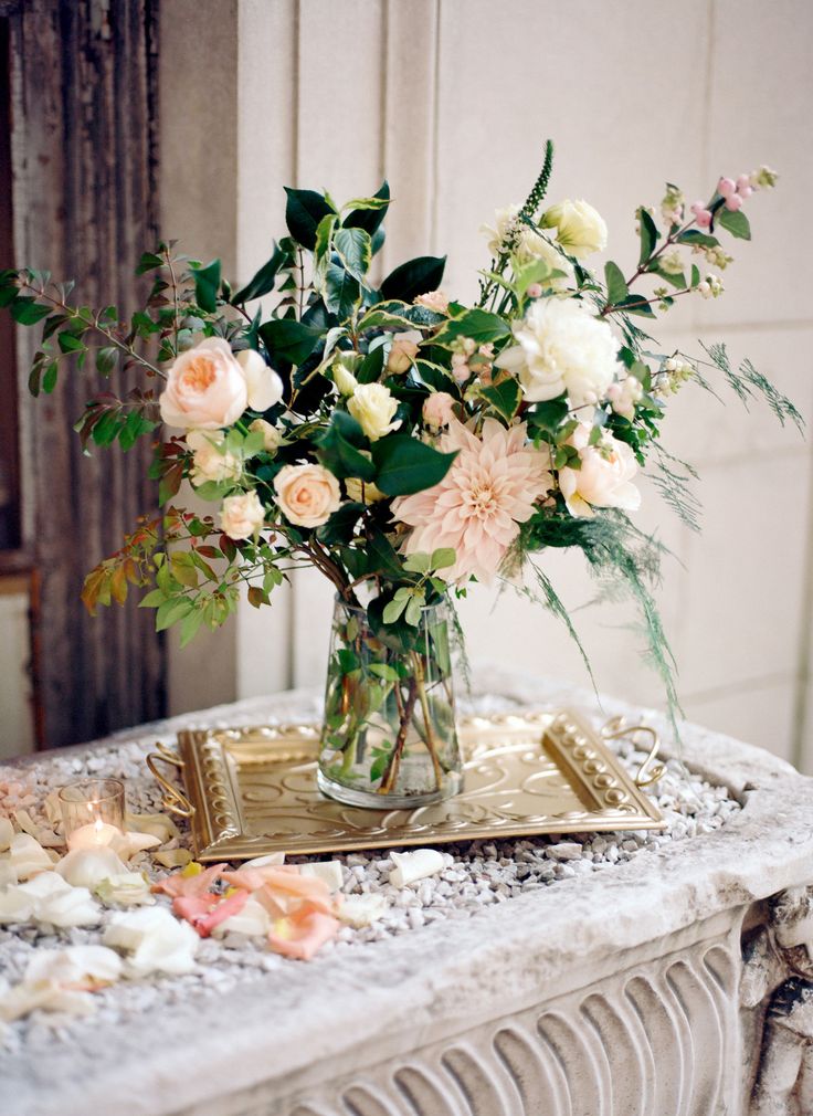 a romantic summer wedding centerpiece of a clear vase with blush blooms and lots of leaves for more texture