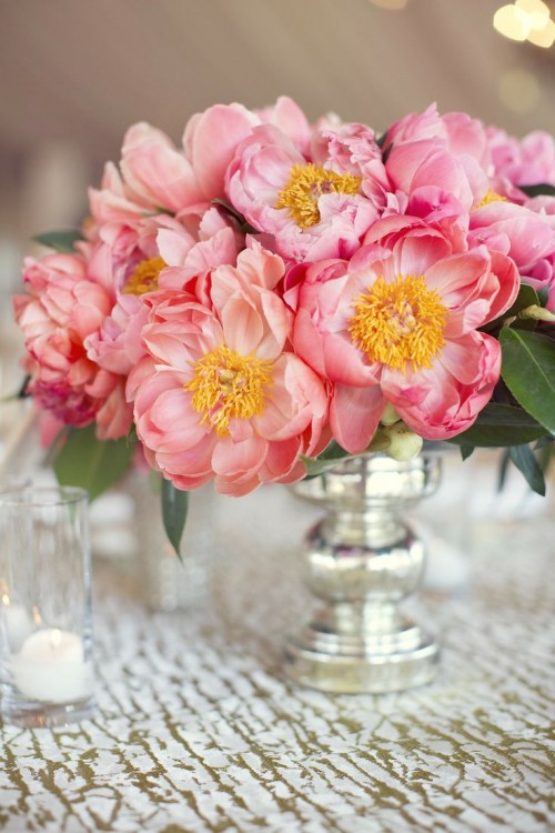 a bright vintage-inspired summer wedding centerpiece of a silver vase and coral blooms with leaves is a lovely and bright idea