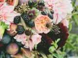a lush wedding centerpiece of blush and peachy blooms, berries, fruit and some greenery looks very lush and bright