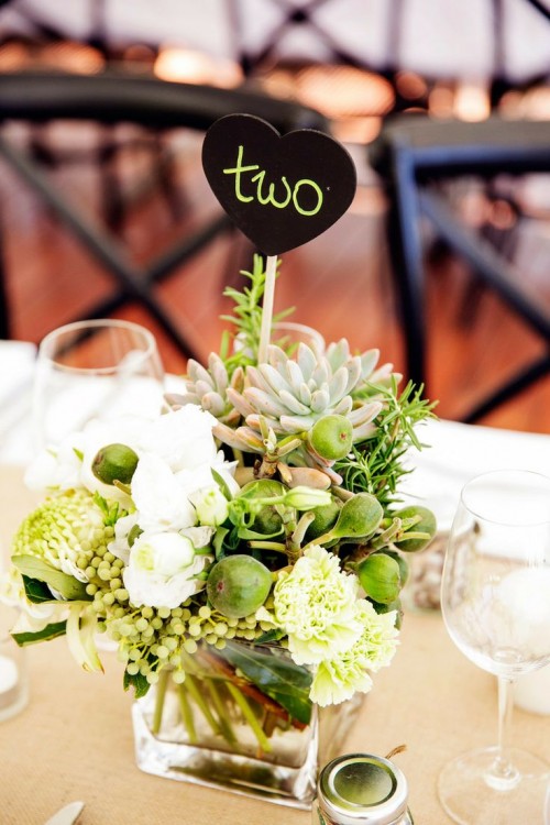 a trendy summer wedding centerpiece of a clear vase, white and green blooms and greenery, succulents and air plants