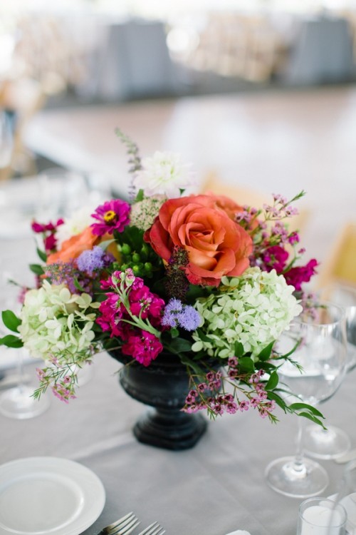 a bright refined wedding centerpiece of a vintage urn, bright orange, fuchsia, purple, green and blue blooms looks lovely