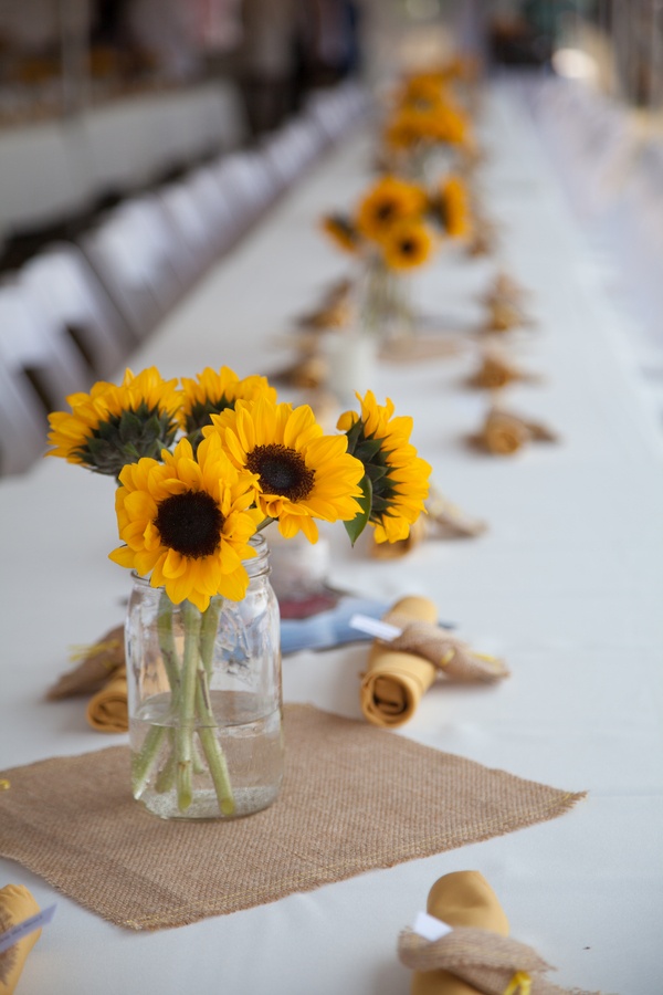 a simple rustic summer wedding centerpiece of a clear jar and sunflowers will add color and a natural feel to the space