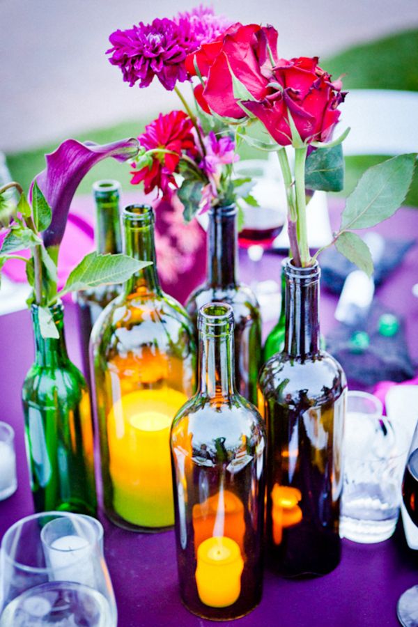 a bold summer wedding centerpiece of wine bottles, bright blooms and greenery and a candle lantern will fit a vineyard summer wedding
