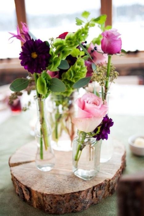 a bright relaxed summer wedding centerpiece of a wood slice, vases and jars, pink and purple blooms and greenery