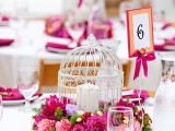 a refined summer wedding centerpiece of a candle in a cage, bright pink and fuchsia blooms and leaves