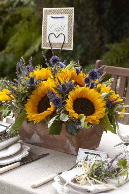 a colorful summer wedding centerpiece of a wooden box, sunflowers, thistles, allium and lavender features much color and texture