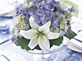 a romantic pastel summer wedding centerpiece of a clear stand with blue and white blooms and foliage is delicate and chic