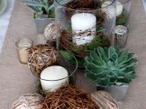 a woodland wedding centerpiece of nuts, vine balls, candles, succulents and candles in tall glasses wrapped with vine