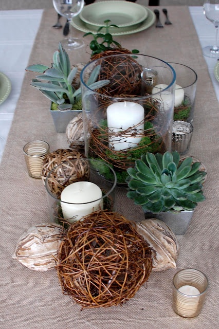 a woodland wedding centerpiece of nuts, vine balls, candles, succulents and candles in tall glasses wrapped with vine