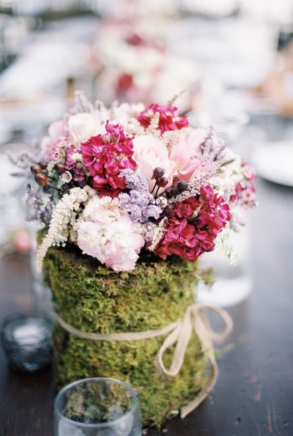 a summer woodland wedding centerpiece of light pink, blush and fuchsia blooms and a vase wrapped in moss