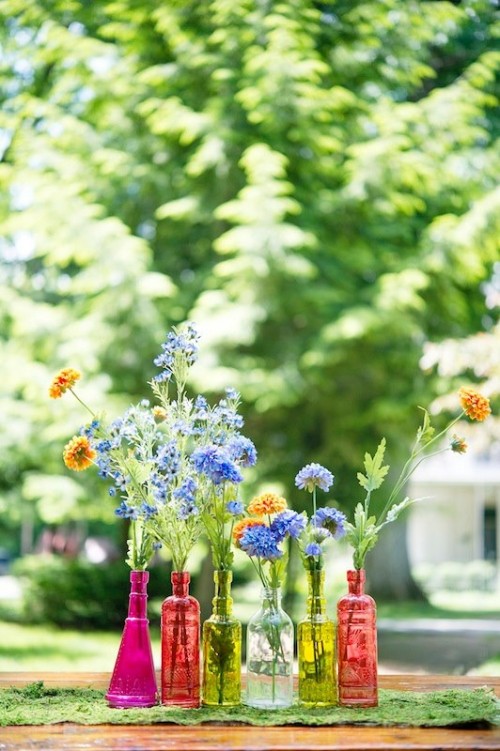a colorful wedding centerpiece of bright glass vases and colorful blooms - orange and blue blooms and greenery