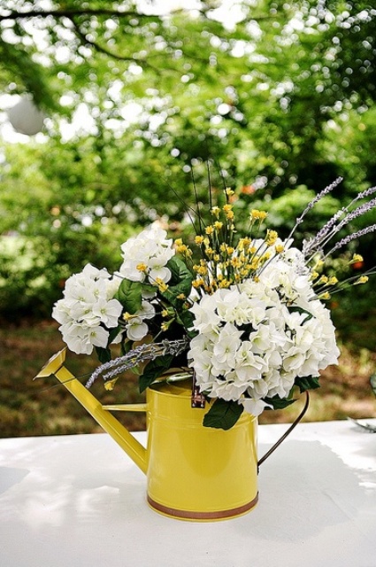 a rustic summer wedding centerpiece of a yellow watering can, white and yellow blooms and some lavender