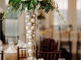 a winter wedding centerpiece of a tall vase filled with ornaments, greenery, twigs and white blooms is ideal for a winter wedding