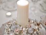 a pretty winter wedding centerpiece of a bowl with shiny Christmas ornaments and a single pillar candle in the middle