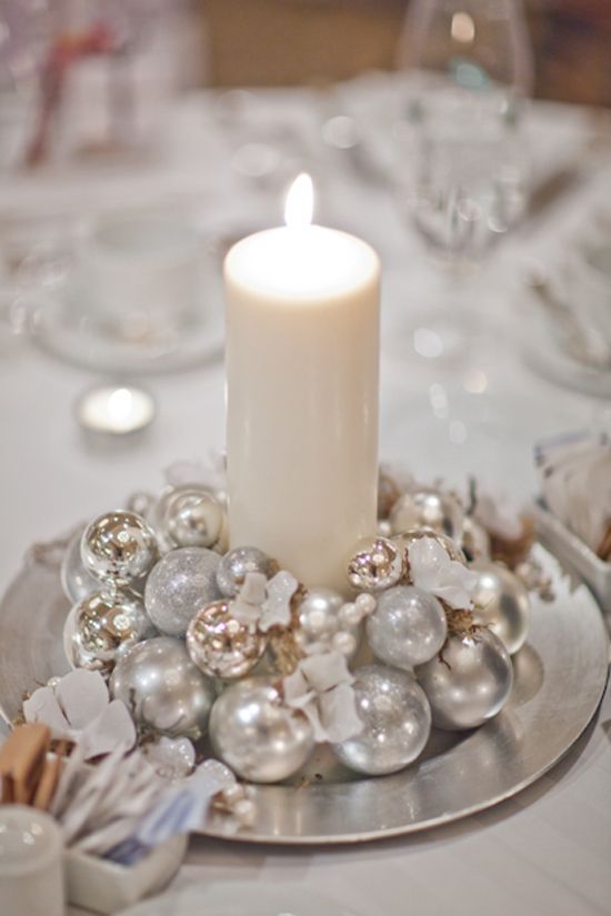 A pretty winter wedding centerpiece of a bowl with shiny Christmas ornaments and a single pillar candle in the middle