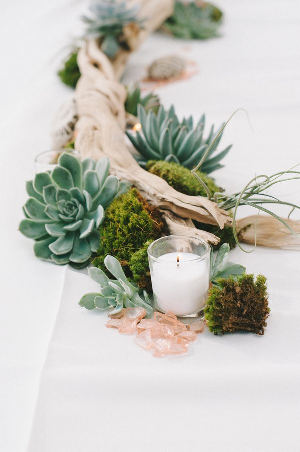 A driftwood wedding centerpiece of moss, succulents, driftwood and candles plus air plants for a coastal wedding