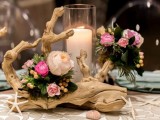 a driftwood wedding centerpiece of blush and pink blooms,greenery, a large candle and starfish