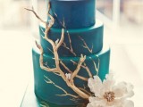 a blue beach wedding cake with gilded driftwood and white blooms is a masterpiece for a coastal or beach wedding