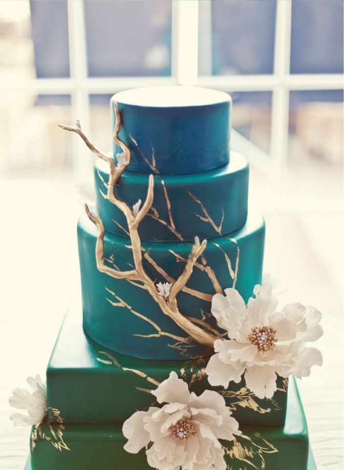 A blue beach wedding cake with gilded driftwood and white blooms is a masterpiece for a coastal or beach wedding