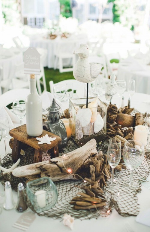 a cool beach wedding decoration of driftwood, candles, seashells, starfish, pebbles, fishnet and bottles