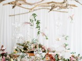 a driftwood wedding decoration hung overhead with glass bubbles with candles and greenery and blooms