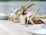 a dirftwood wedding centerpiece of greenery and pink blooms plus some candles is a stylish idea