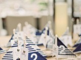 mini favors and escort cards of driftwood sailboats with navy and white decor and table numbers on them