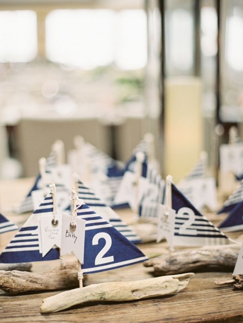 mini favors and escort cards of driftwood sailboats with navy and white decor and table numbers on them