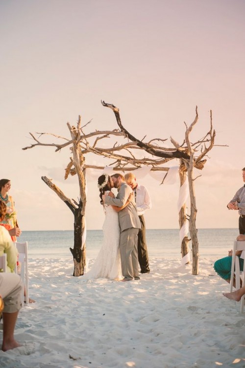 a driftwood wedding arch with white fabric is amazing for a coastal or beach wedding