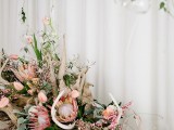 a lush beach wedding centerpiece of driftwood, pink tulips and king proteas, greenery and succulents