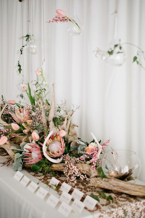 a lush beach wedding centerpiece of driftwood, pink tulips and king proteas, greenery and succulents