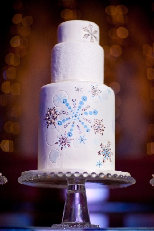 a white wedding cake decorated with blue and copper snowflakes on one tier is a lovely idea for a winter wedding