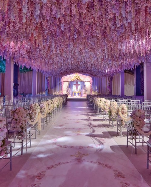 a breathtaking wedding ceremony space with flower garlands hanging over the space, flower arrangements on the chairs and flwoer petals is wow