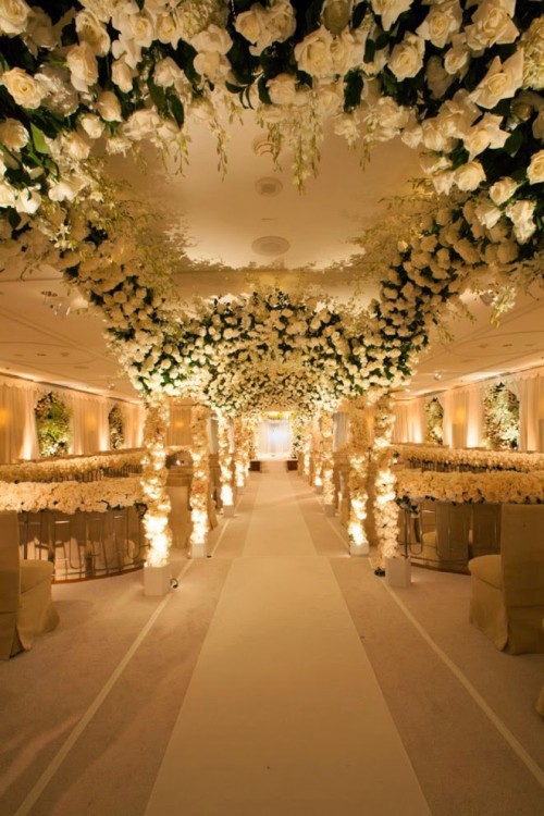 an unbelievable wedding ceremony space done with lots of white roses covering the ceiling, the benches and linin up the aisle is extremely sophisticated