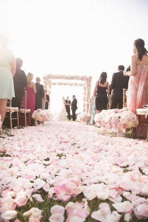 a wedding arch fully covered with pink roses and peony roses and a wedding aisle fully covered with their petals for a romantic feel