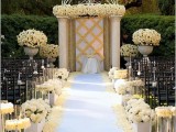 an exquisite wedding ceremony space done with lots of white rose arrangements and a wedding backdrop covered with white roses on top